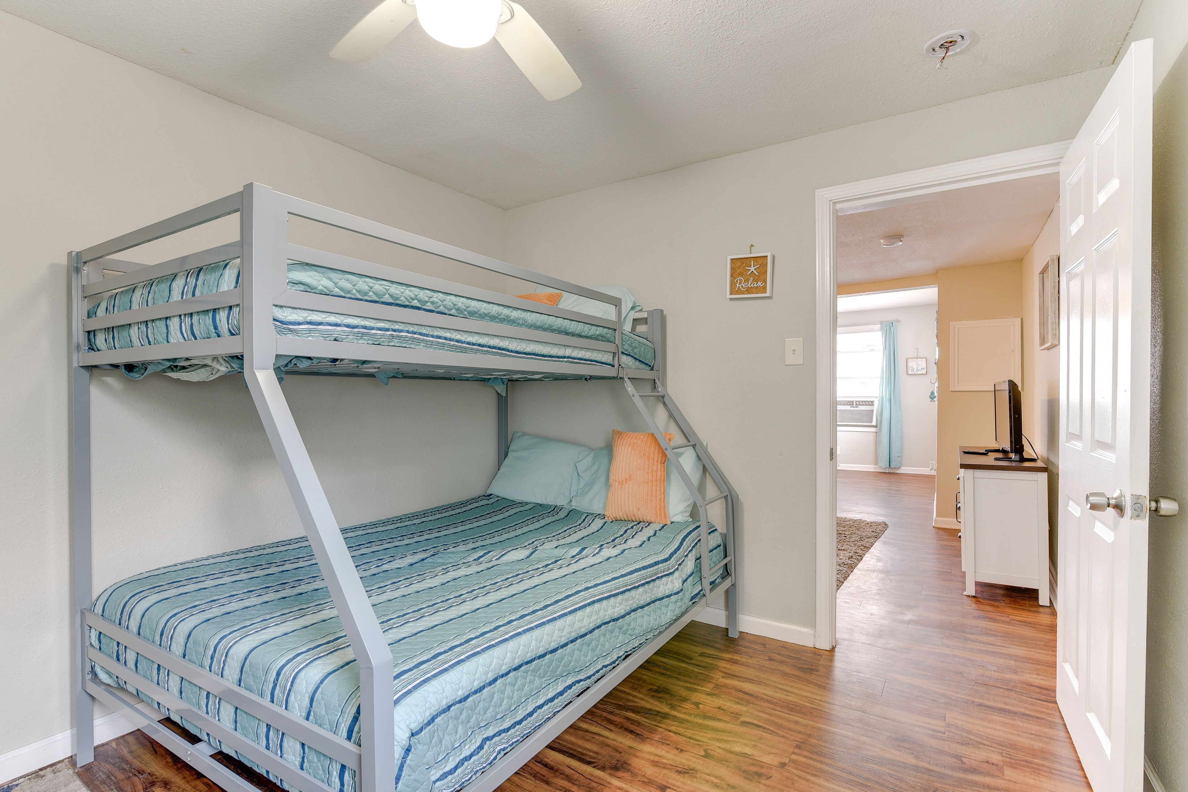 A bunk bed with striped bedding, a ceiling fan, and a hallway leading to a kitchen area.