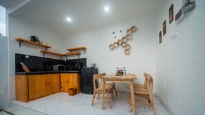 A compact kitchen with wooden cabinets, a black countertop, and a dining area with a wooden table and chairs. - MODERN COZY PRIVATE 2BR VILLA WITH ROOF TOP SUNSET VIEW (Bali)