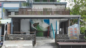 A building with a surf-themed mural, a stone wall, and a sign indicating a surf guesthouse. - LowPressure Surf Guesthouse (Donghe)