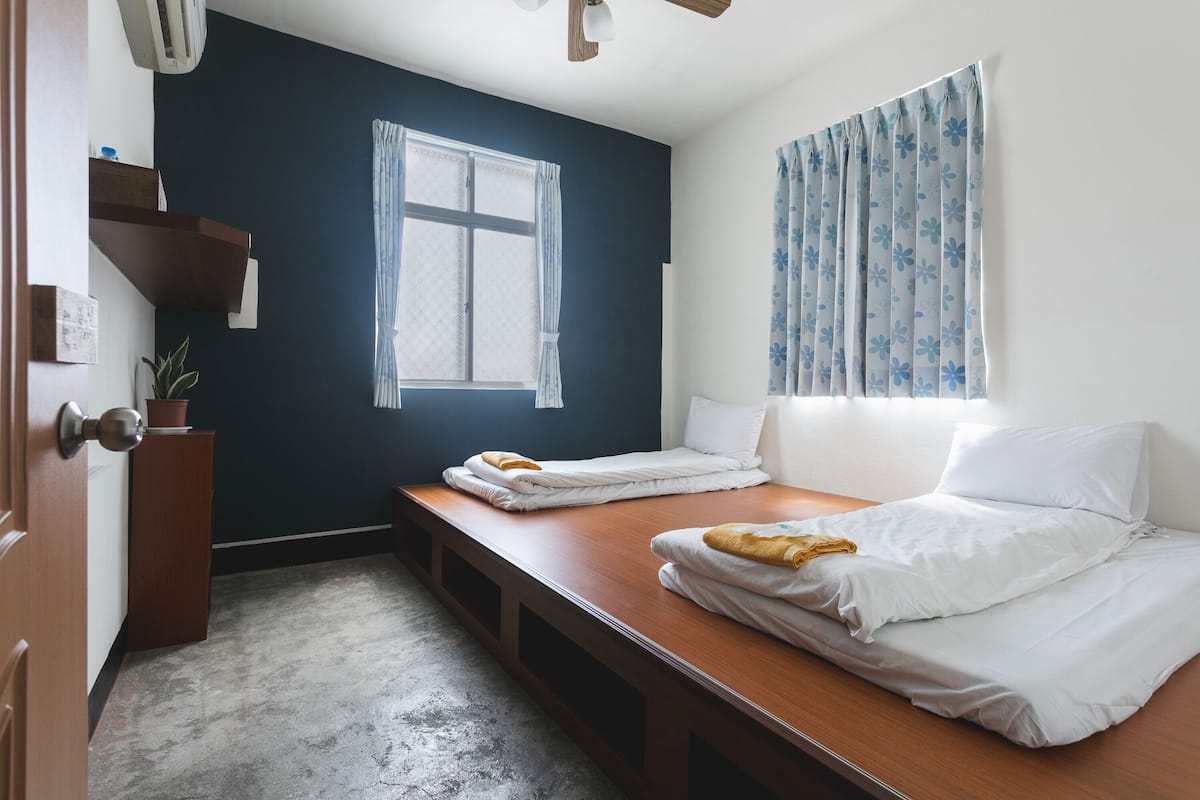 A bedroom with two beds, a window with curtains, a ceiling fan, and a small plant.