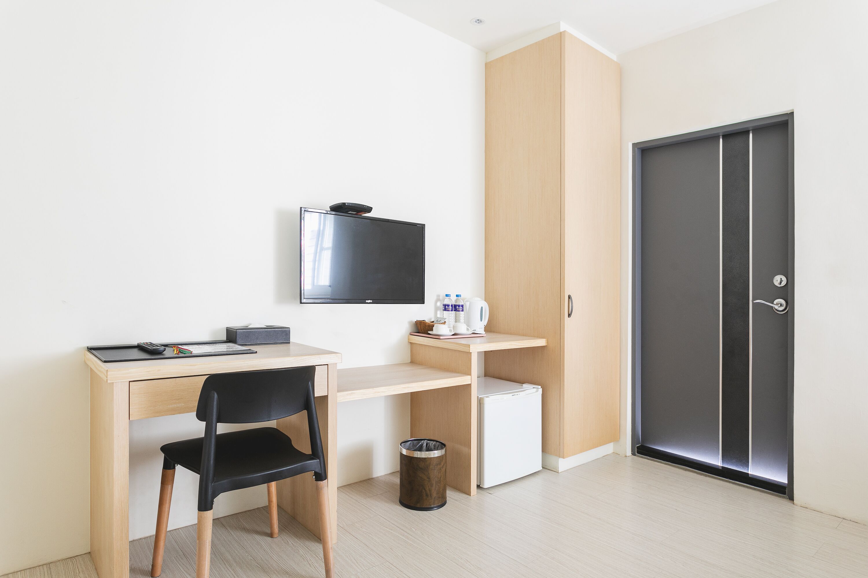 A compact room with a desk, chair, TV, wardrobe, and a door.