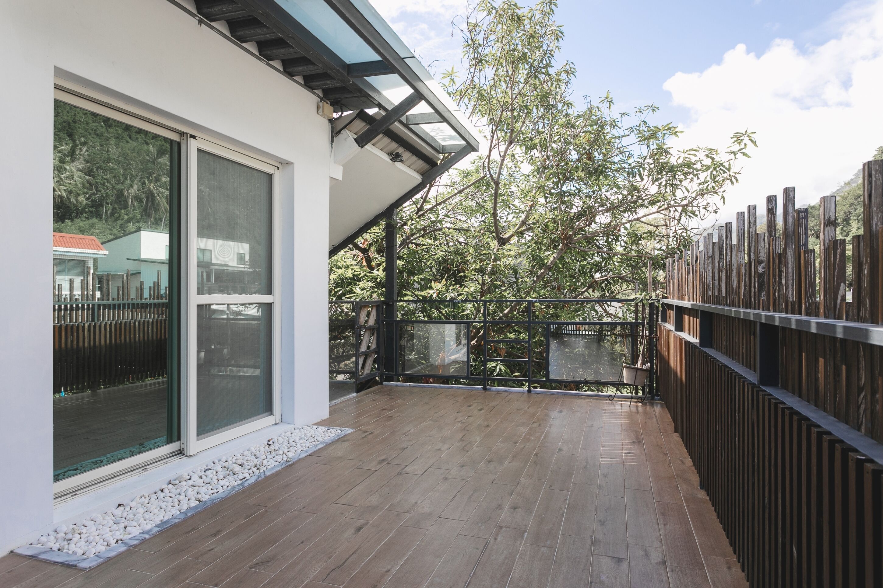 A covered patio with a wooden floor, a glass door, and a wooden fence.