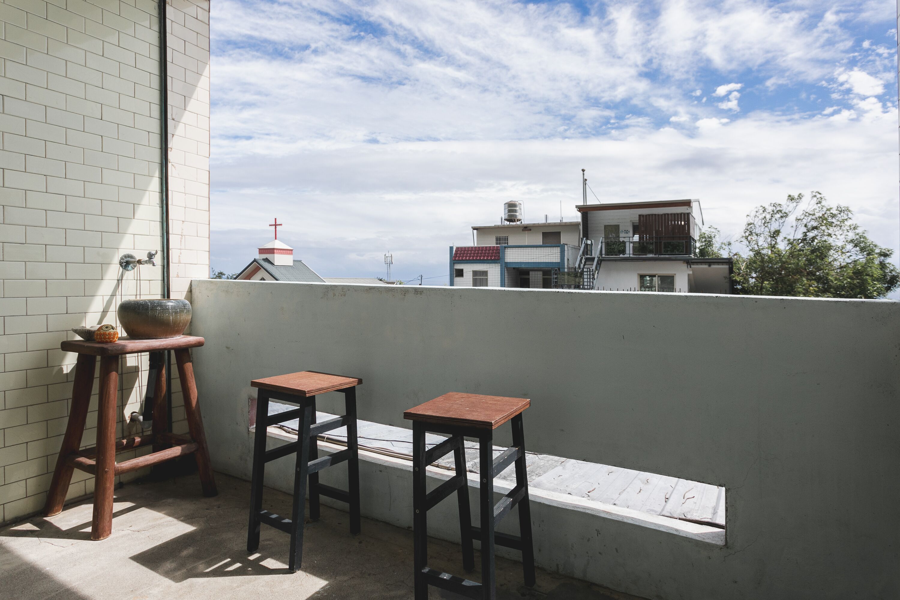 A balcony with two wooden stools and a large ceramic pot.