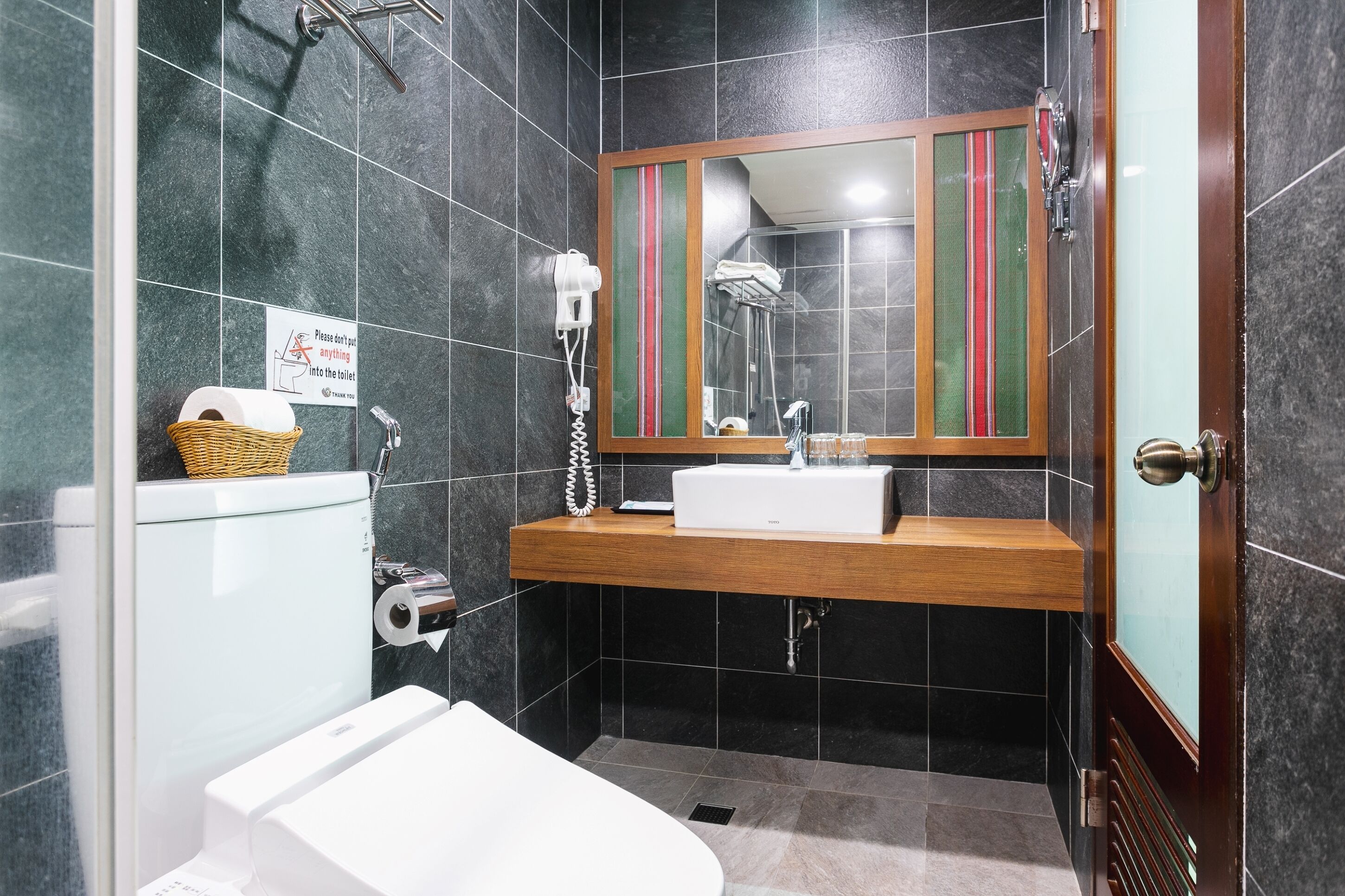A modern bathroom with a glass shower enclosure, a wooden vanity, a white sink, and a toilet.