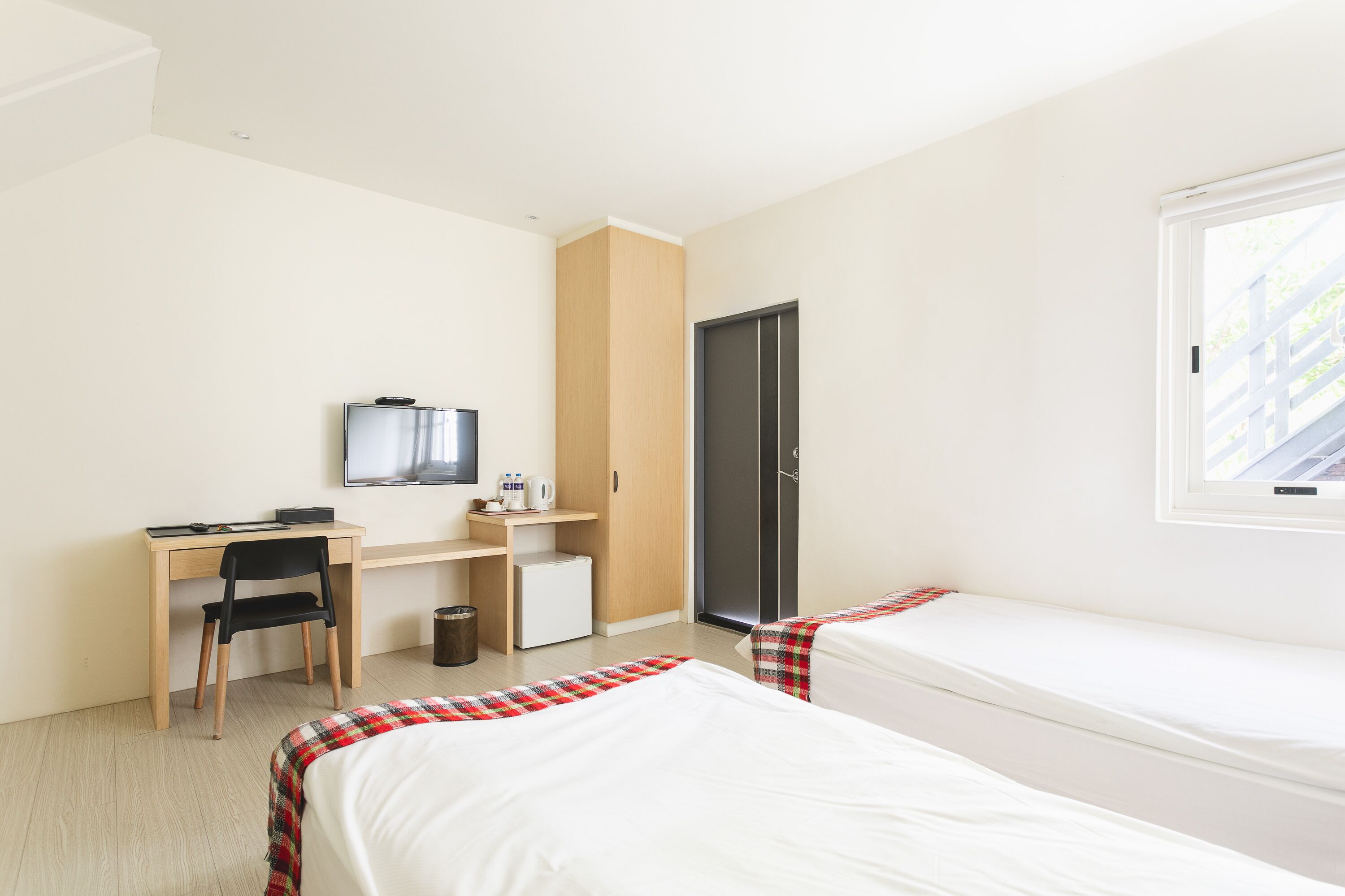 Ein Hotelzimmer mit einem Bett, einem Schreibtisch, einem Stuhl, einem kleinen Kühlschrank und einem Fenster.