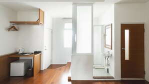 A modern, minimalist room with a wooden floor, a small kitchenette, a wooden cabinet, a white radiator, and a door leading to another room. - LowPressure Surf Guesthouse (Donghe)