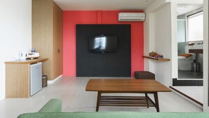 A compact living space with a kitchenette, a flat-screen TV mounted on a black wall, a wooden table, and a green rug. - LowPressure Surf Guesthouse (Donghe)