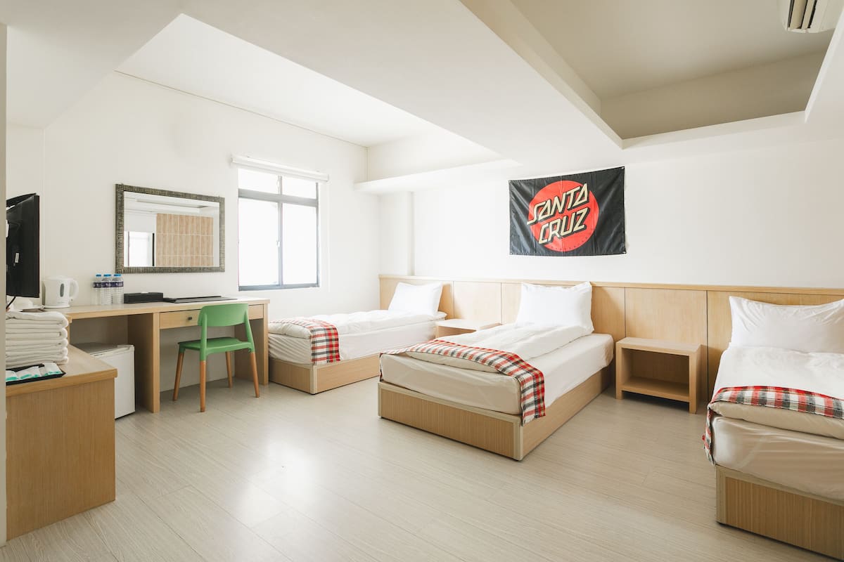 A hotel room with two beds, a desk, a chair, and a TV.