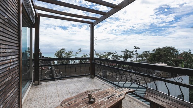 A balcony with a view of the sea, a wooden bench, and a metal railing. - LowPressure Surf Guesthouse (Donghe)