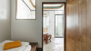 A hotel room with a bed, a wooden bench, a table with chairs, and a view through an open door to a balcony. - LowPressure Surf Guesthouse (Donghe)