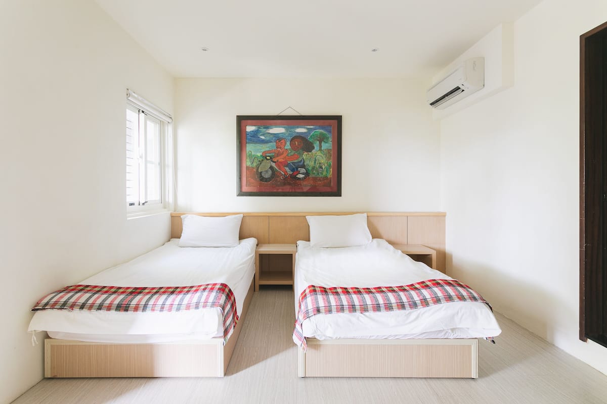 A room with two beds, a painting on the wall, and an air conditioning unit.