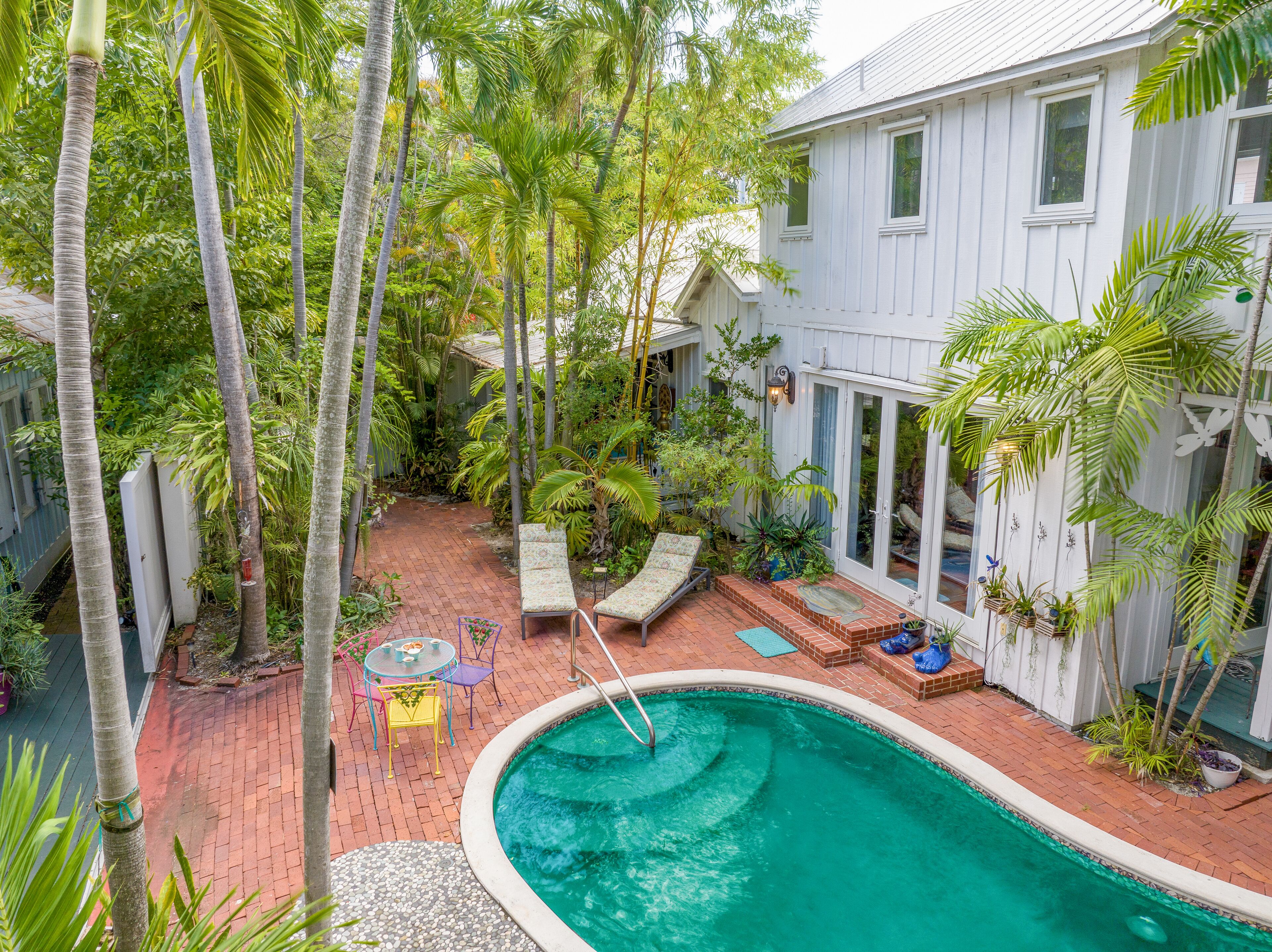 A backyard with a swimming pool, patio furniture, and lush greenery.