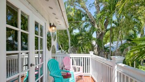 Une véranda couverte avec des balustrades blanches, deux fauteuils Adirondack turquoise et une plante en pot.