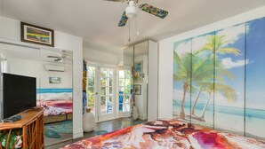 Une chambre à coucher ornée d’une fresque murale sur le thème de la plage, d’un téléviseur posé sur un meuble en bois et d’une grande fenêtre donnant sur l’extérieur.
