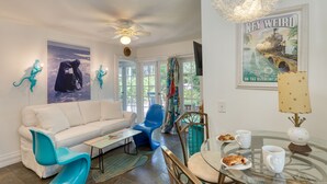 Un salon moderne avec un canapé blanc, des fauteuils bleus, une table basse en verre et un coin repas comprenant une table et des chaises.