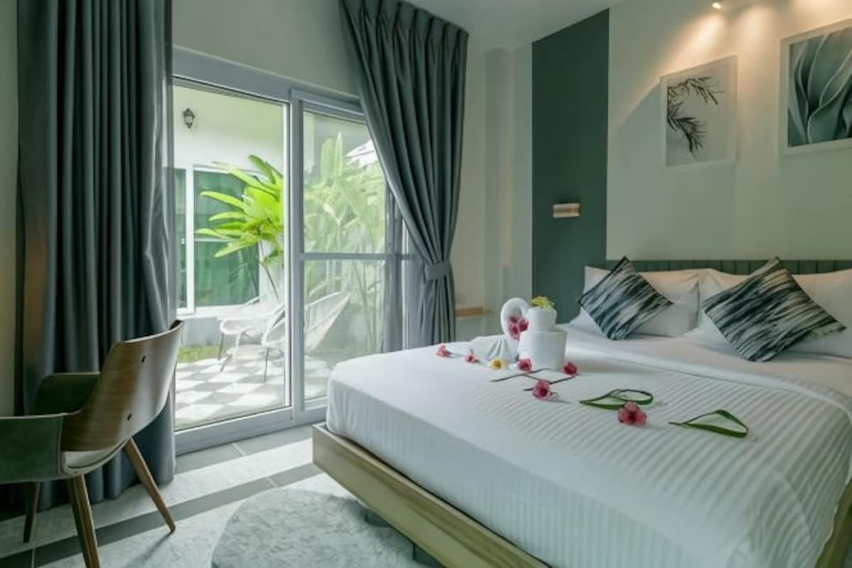 A bedroom with a bed, a chair, a window with curtains, and a view of greenery.