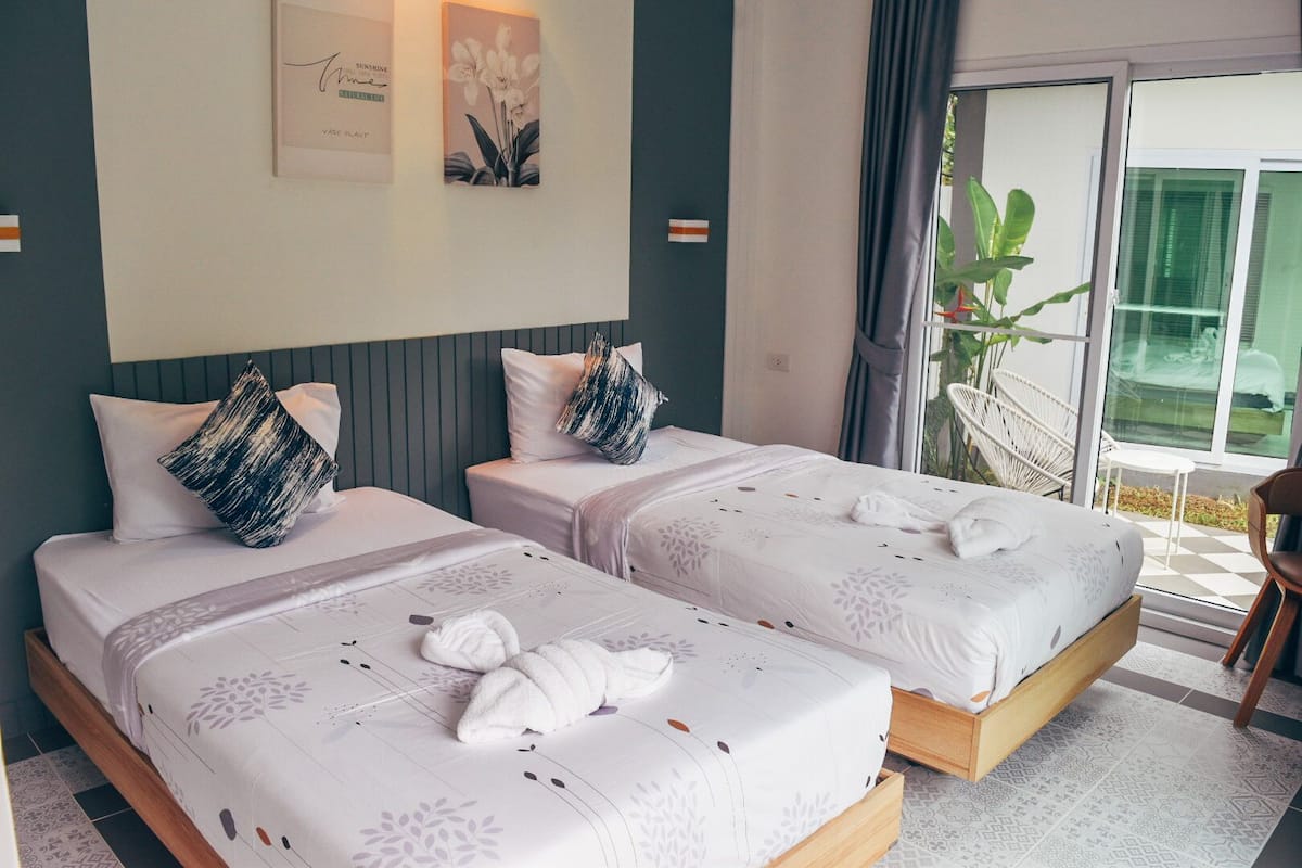 A hotel room with two beds, each with a pillow and a towel. There is a window with a view of greenery outside.