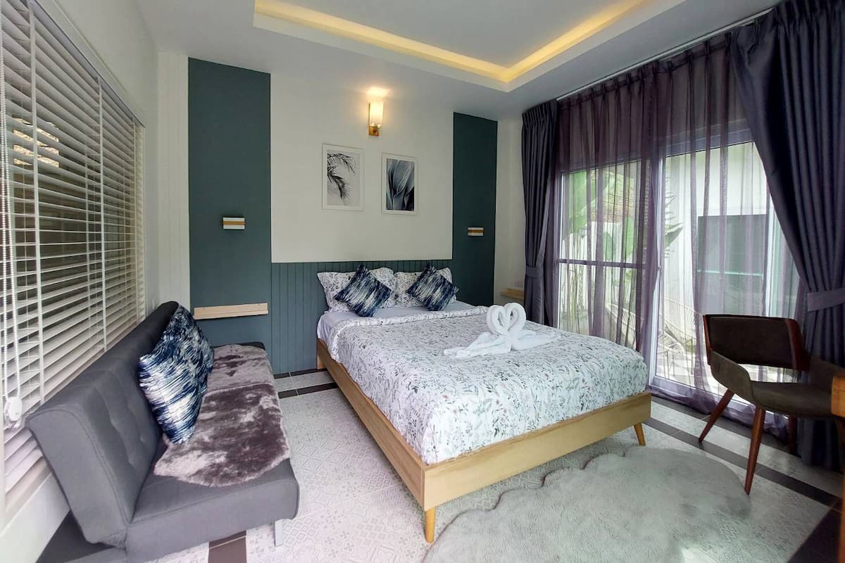 A modern bedroom with a large bed, a sofa, a chair, and a window with curtains.