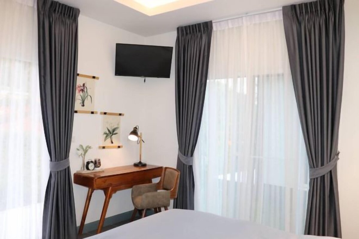 Une chambre d’hôtel avec un lit, un bureau et une chaise, un téléviseur fixé au mur et des rideaux aux fenêtres.