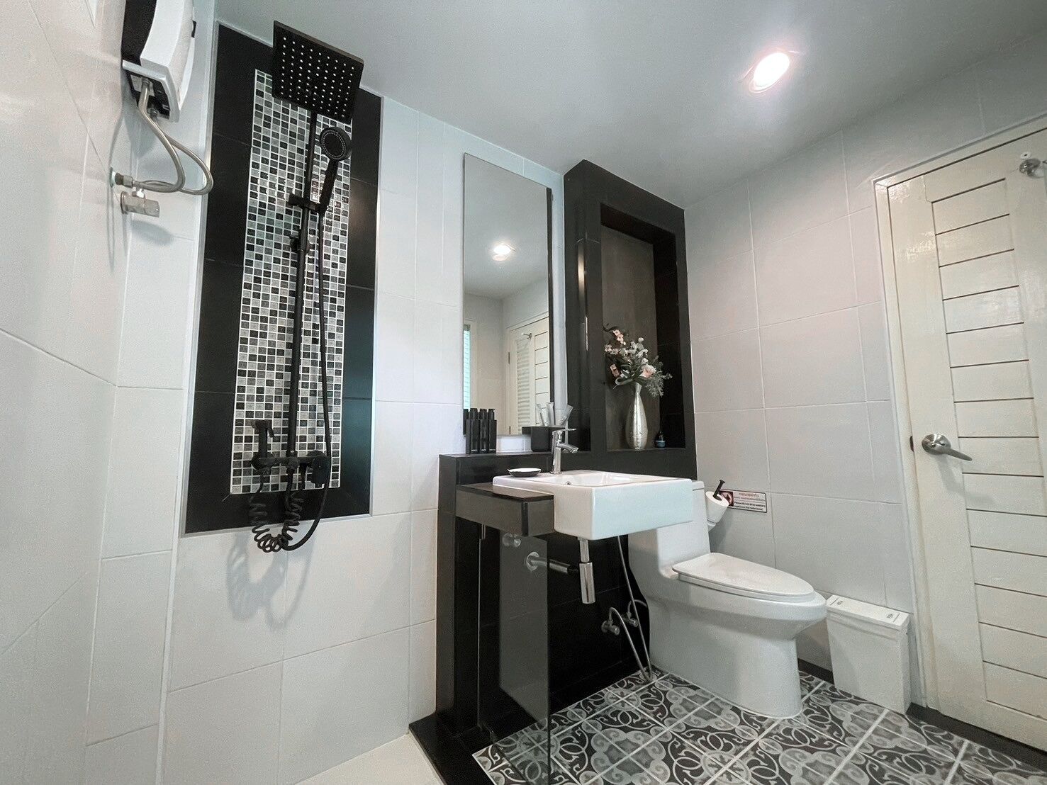 Un baño moderno con piso de baldosas blanco y negro, un lavamanos blanco, un inodoro y una ducha con cabezal negro.