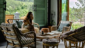 Une pièce meublée de mobilier en osier, dotée d’un ventilateur et offrant une vue sur la verdure.