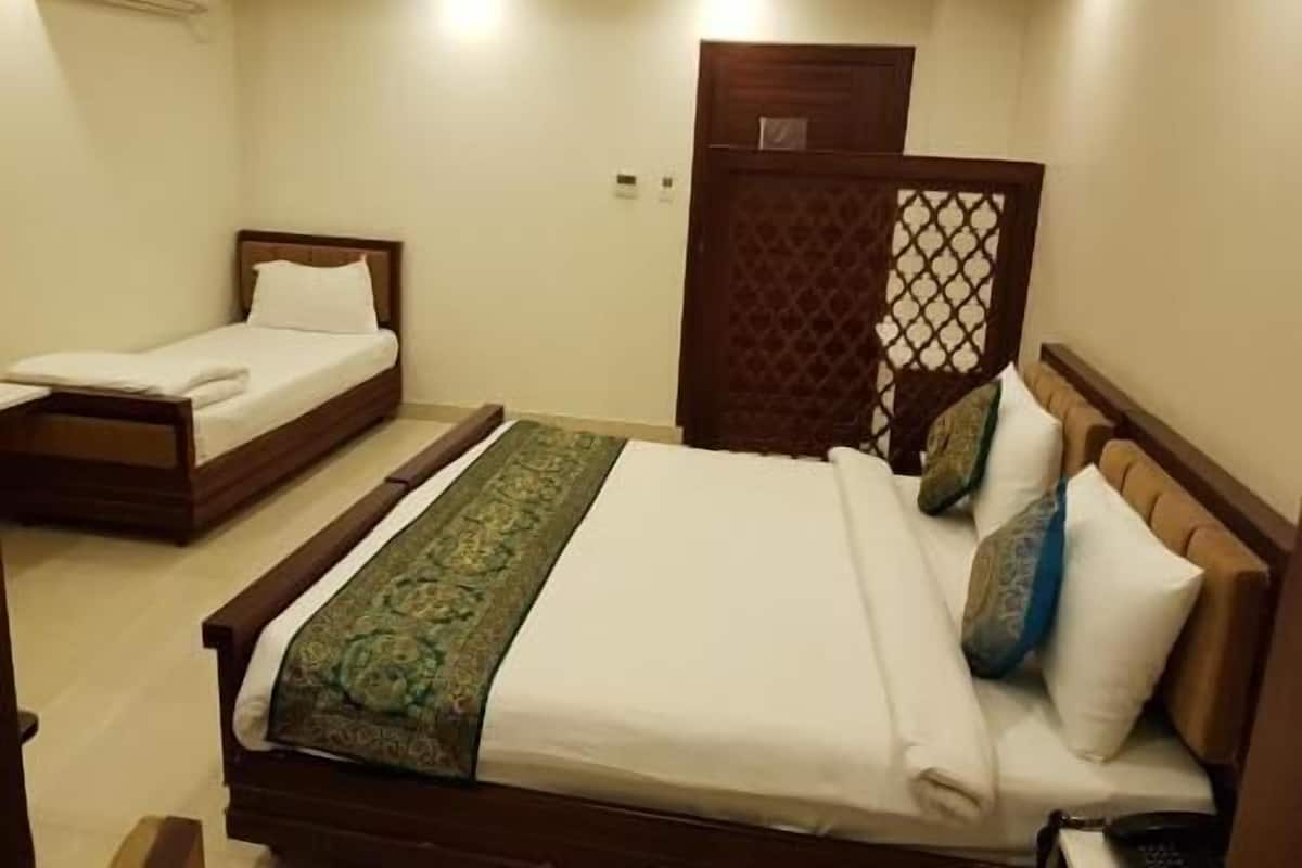 Ein Hotelzimmer mit zwei Einzelbetten, einem großen Bett mit gemustertem Überwurf und einem hölzernen Kopfteil.