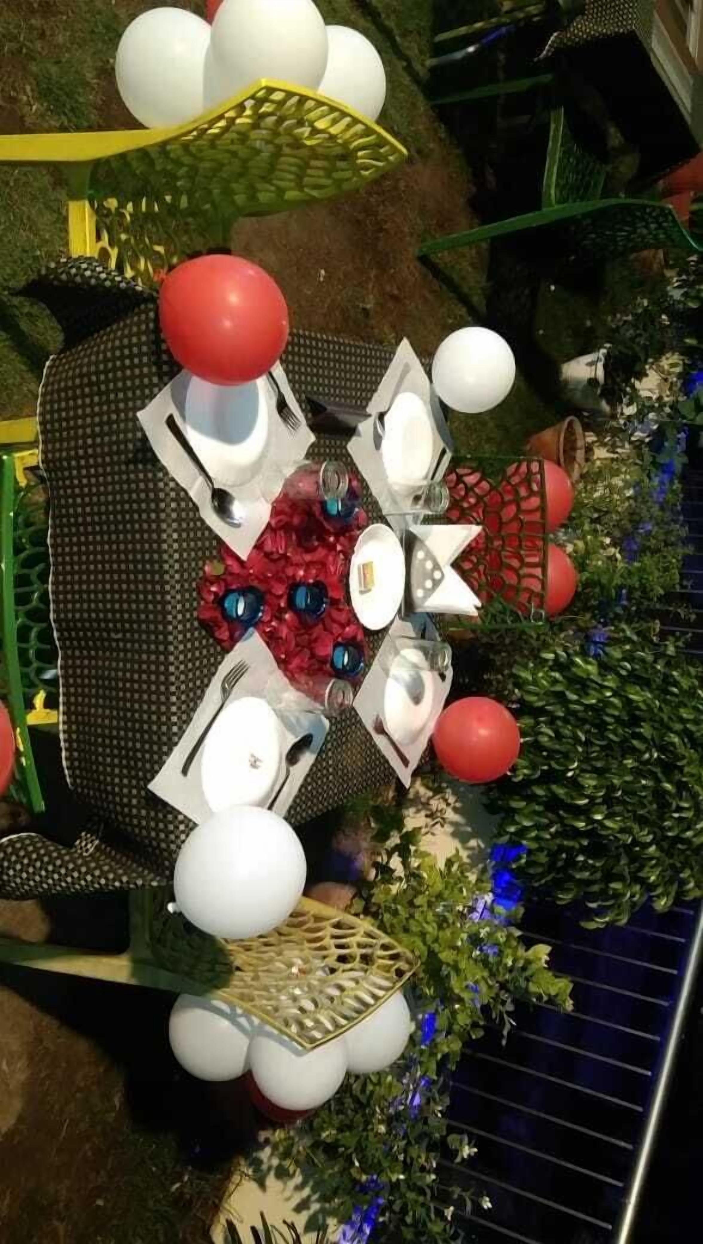 Un espace de restauration en plein air avec une table ronde, des ballons blancs et rouges, et un centre de table décoratif.