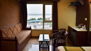 A small, cozy room with a sofa, a dining table, and a view of a body of water through a large window. - Hotel Banaras Haveli (Varanasi)