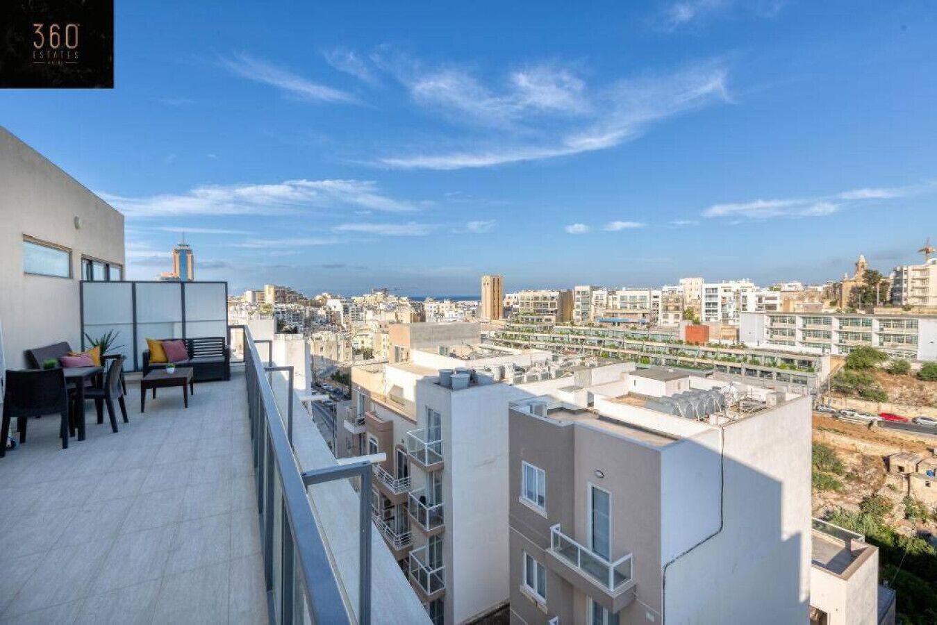 A rooftop terrace with a view of the cityscape, including buildings and a distant view of the sea.