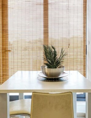 A dining table with a metal bowl and a plant, set against a window with blinds.