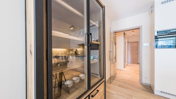 Una cocina moderna con un armario de vidrio, suelo de madera y electrodomésticos integrados.