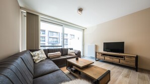 Una sala de estar moderna con un sofá de cuero, una mesa de centro de madera y un televisor de pantalla plana sobre un mueble de madera.