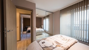 Un dormitorio moderno con una cama grande, una puerta corrediza que da a otra habitación y un ventanal con persianas.