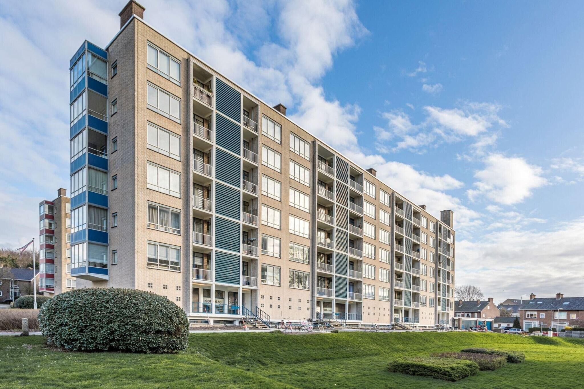 A multi-story residential building with balconies, a well-maintained lawn, and bicycles parked outside.