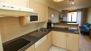 A compact kitchen with a microwave, stove, and sink. There is a small seating area with a sofa and a television. - Stay by the coastal trails, Middelkerke (Middelkerke)