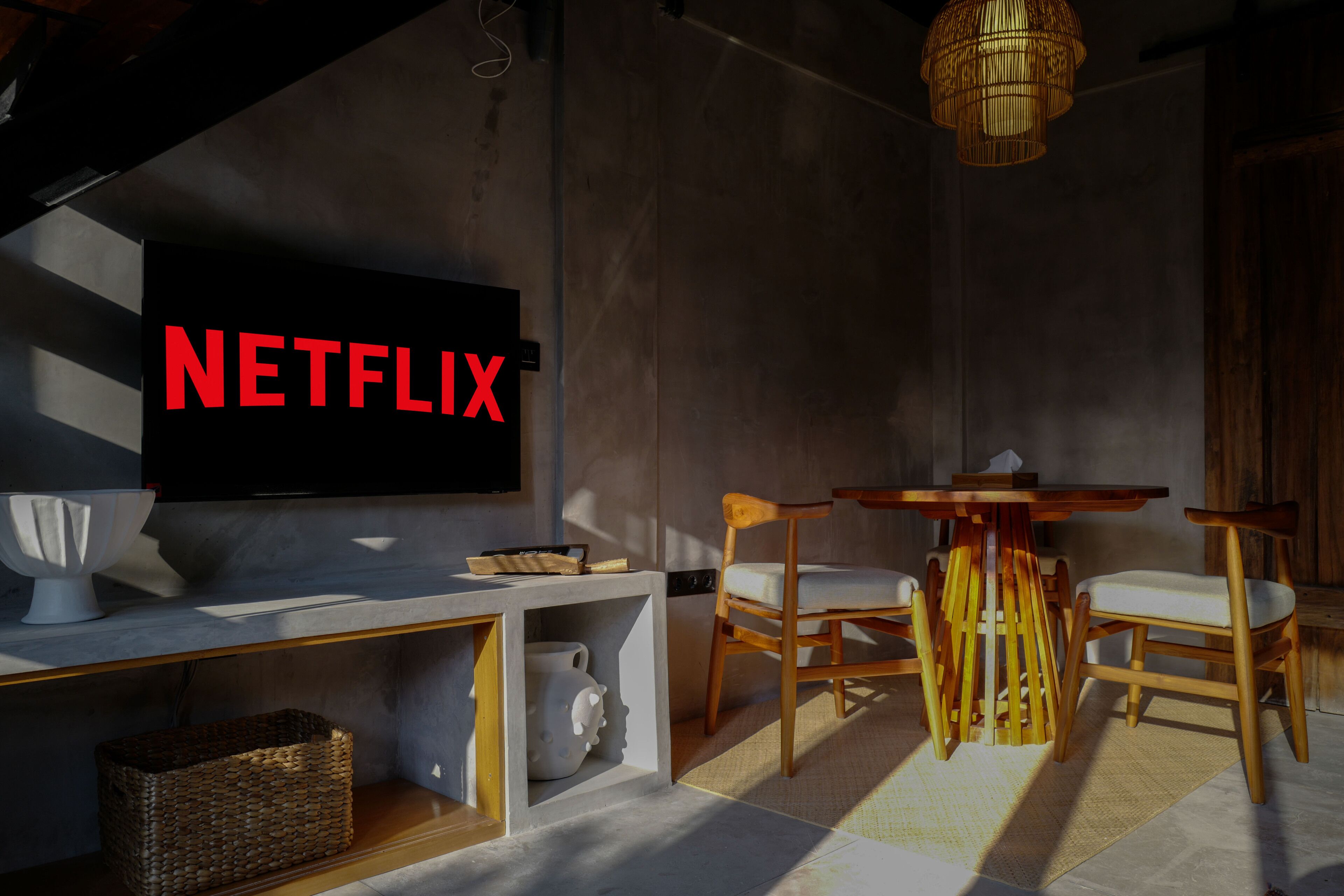 A modern living room with a large flat-screen TV mounted on the wall, wooden dining table, and chairs.