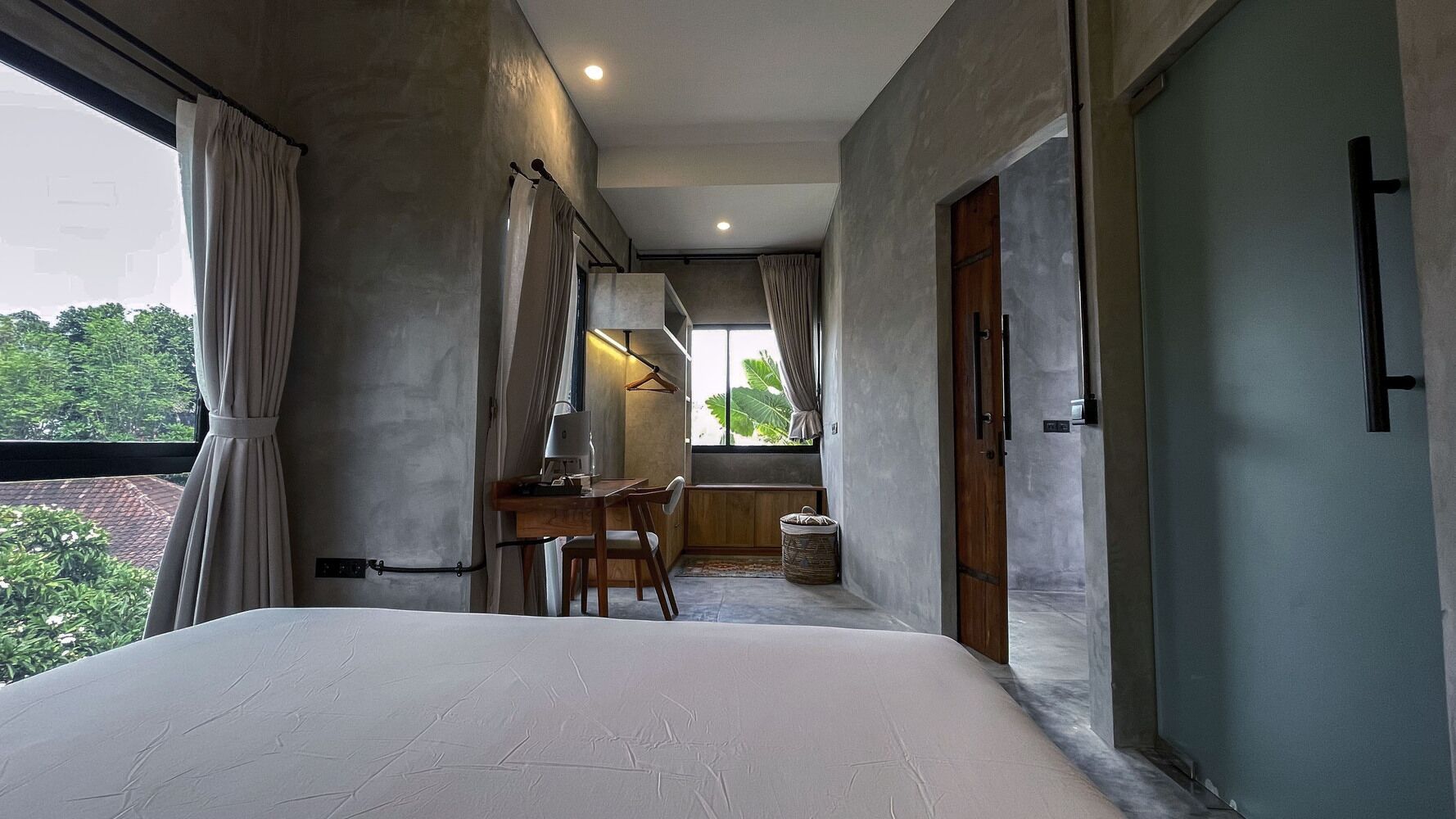 A bedroom with a large bed, a desk with a chair, and a view of greenery outside.