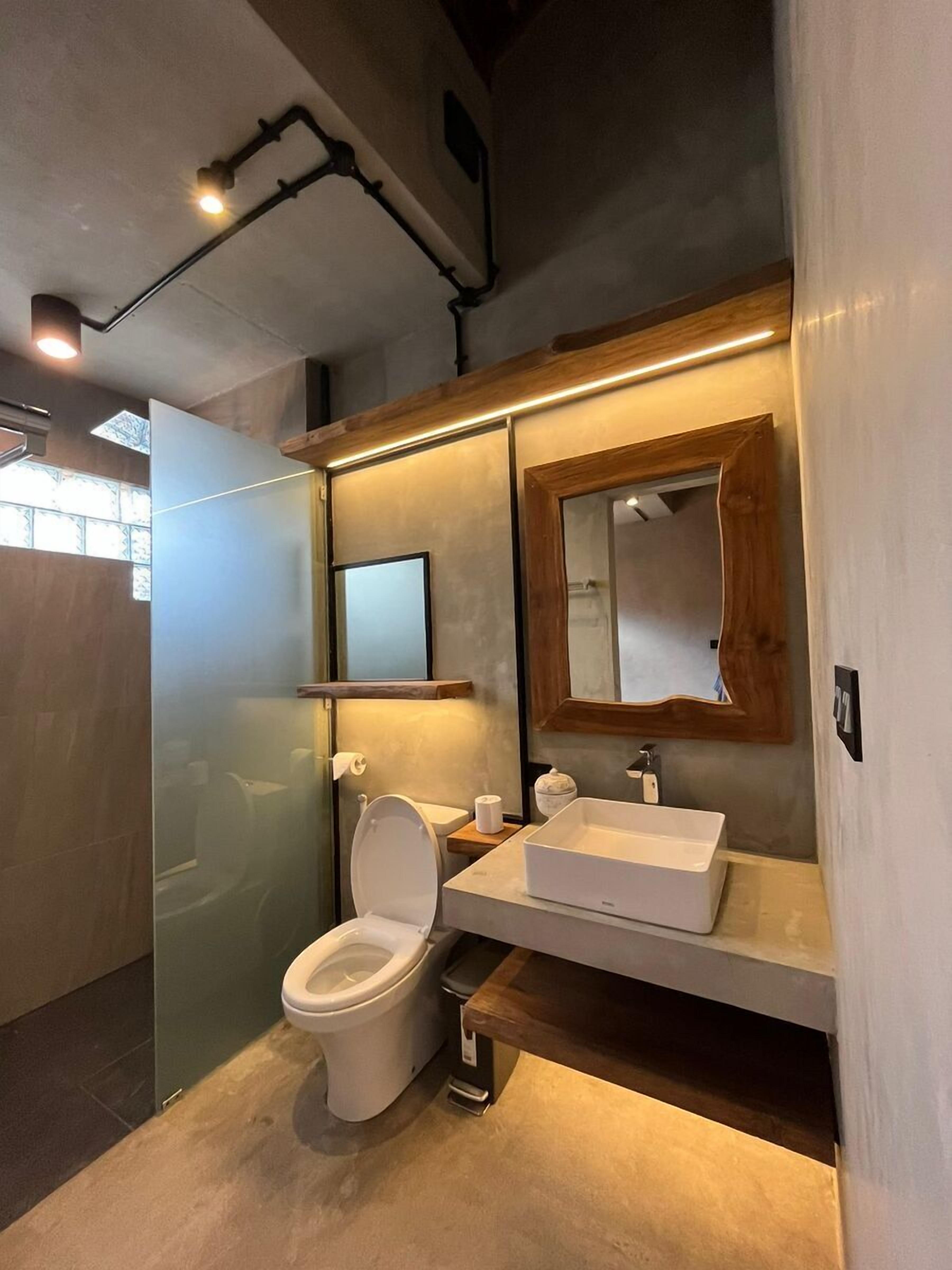 Ein modernes Badezimmer mit einer Duschkabine aus Glas, einer weißen Toilette, einem hölzernen Waschtisch mit Spiegel und einem weißen Waschbecken.