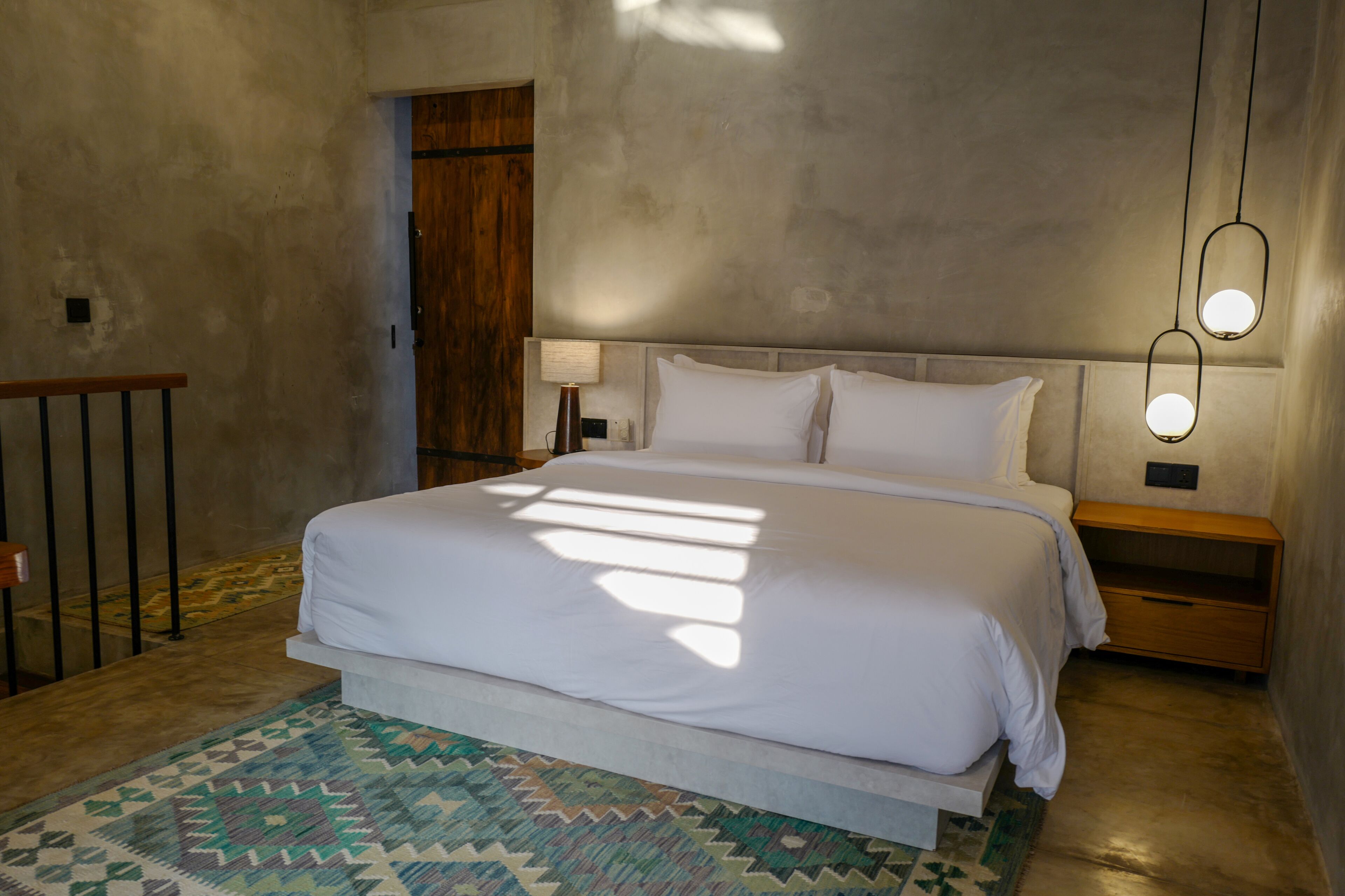 A bedroom with a large bed, a wooden door, and a nightstand with a lamp.