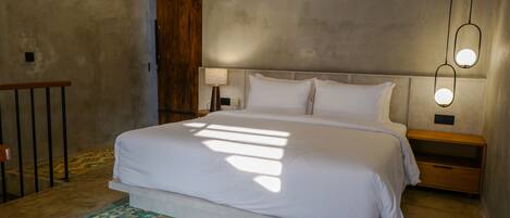 A bedroom with a large bed, a wooden door, and a nightstand with a lamp.