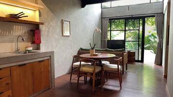 A modern kitchen with wooden cabinets, a dining area with a round table and chairs, and a large window with a view of greenery.