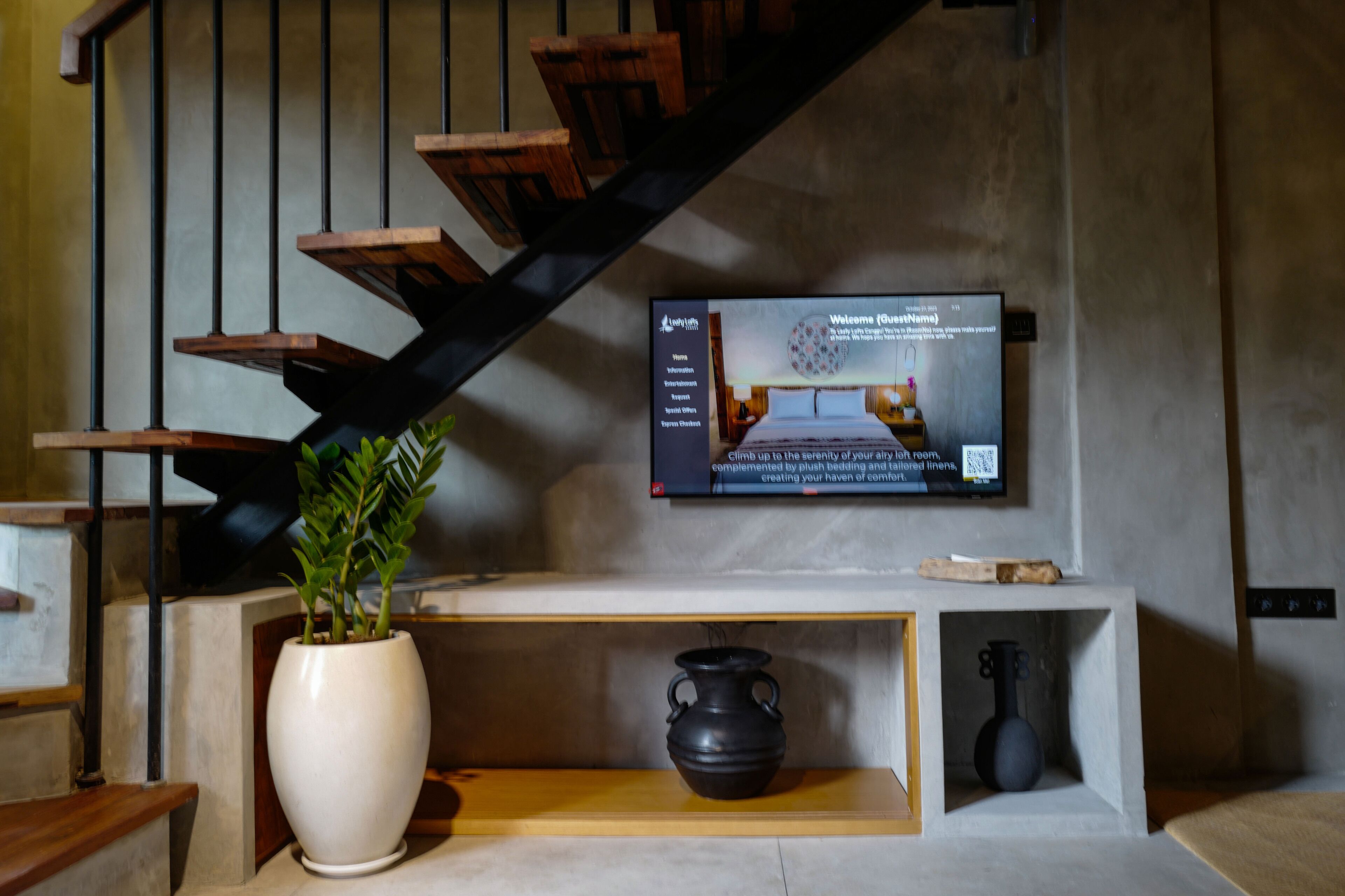 A modern interior with a staircase, a flat-screen TV, a potted plant, and a console table with decorative items.