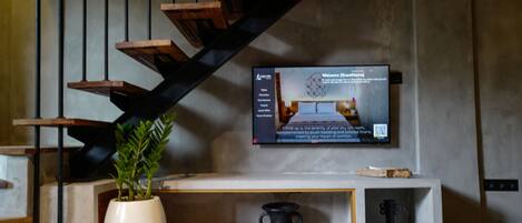 A modern interior with a staircase, a flat-screen TV, a potted plant, and a console table with decorative items.