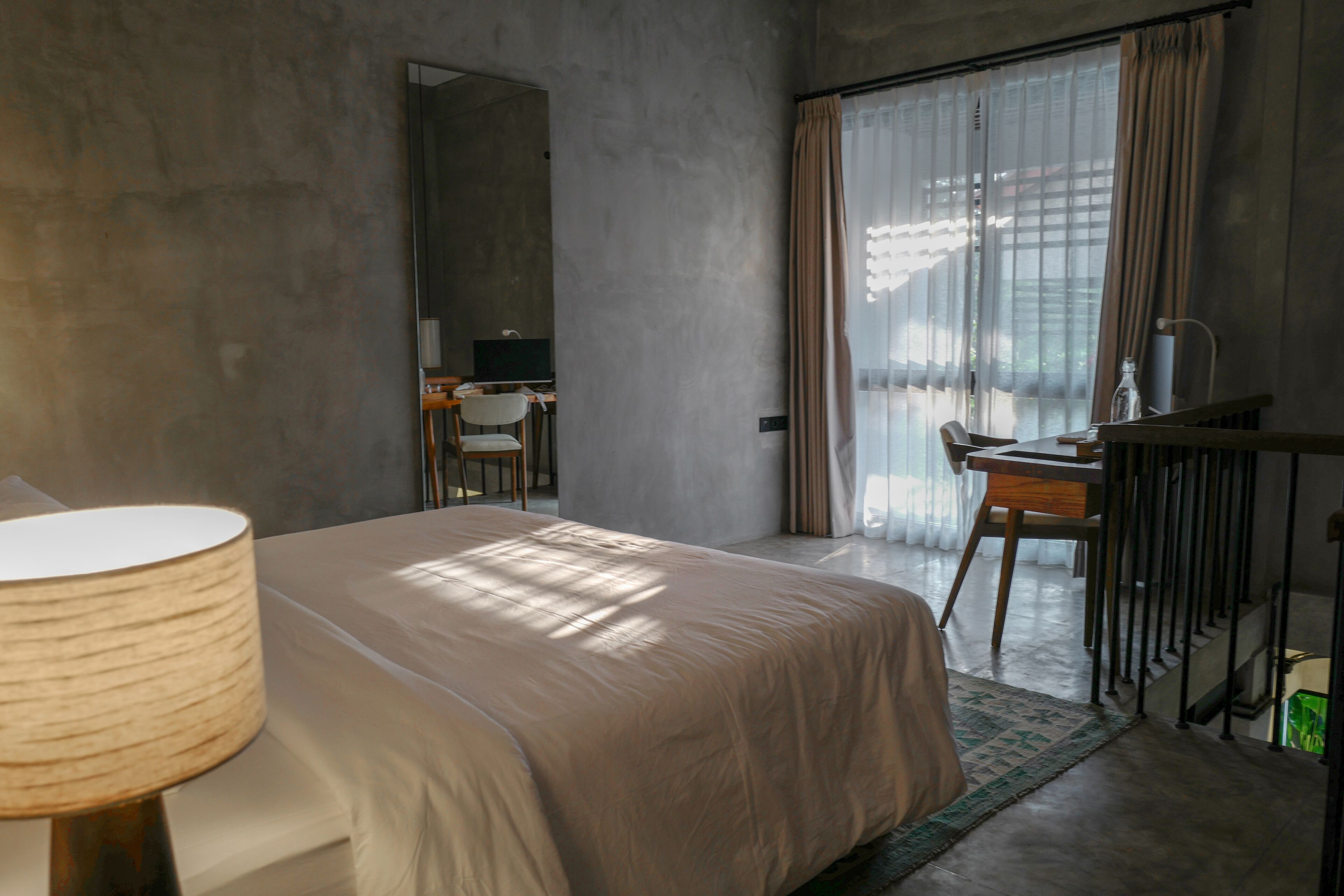Une chambre d’hôtel avec un lit, un bureau, une chaise, une lampe et une vue par la fenêtre.