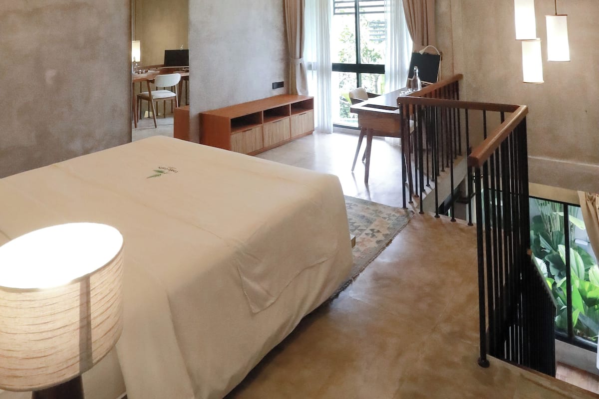 A modern bedroom with a large bed, a desk, and a staircase leading to a balcony.