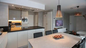 Eine moderne Küche mit einer zentralen Kochinsel, einem Essbereich mit Tisch und einem an der Wand befestigten Fernseher.