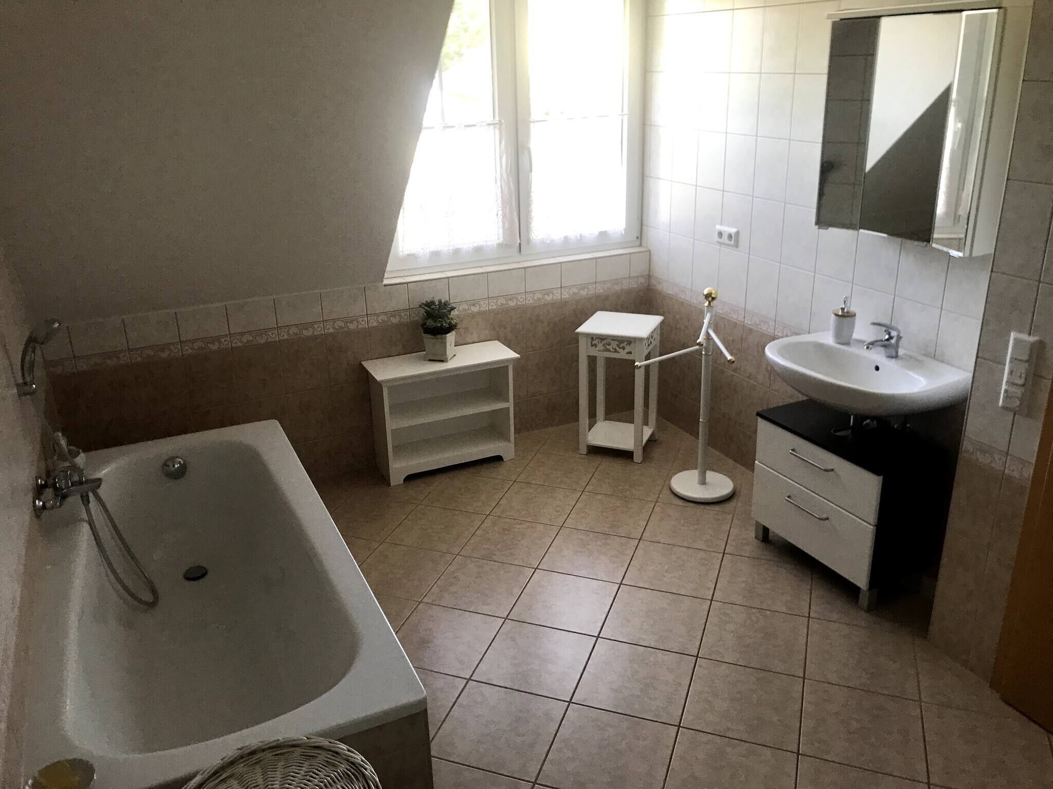A bathroom with a bathtub, a sink, a small table with a plant, and a mirror on the wall.