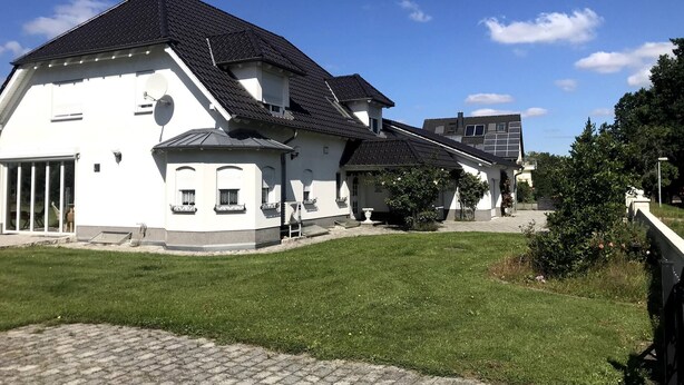 A white building with a black roof, a satellite dish, and a paved courtyard. - Room-haus Im Grünen House in the Green (Neuzelle)