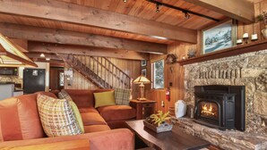 Ein gemütliches Wohnzimmer mit Kamin aus Stein, Holzbalken und einer Treppe zu einer weiteren Ebene.