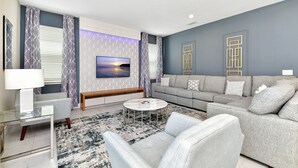 A modern living room with a grey sofa, a glass coffee table, and a patterned rug. - Modern Home near Disney: Private Pool, Ping Pong & Waterpark - 7758WL (Kissimmee)